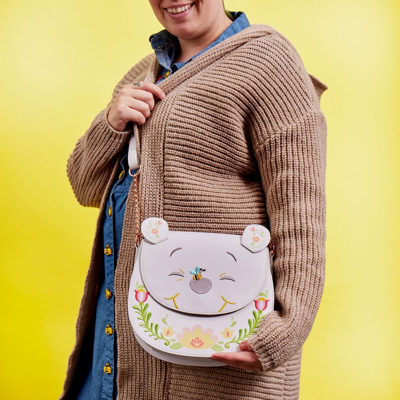 Person wearing a blue top and beige cardigan wearing the Winnie the Pooh Folk Floral Crossbody against a yellow background